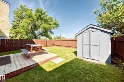 Private fenced yard featuring a wooden deck, a storage shed, and a manicured lawn - 