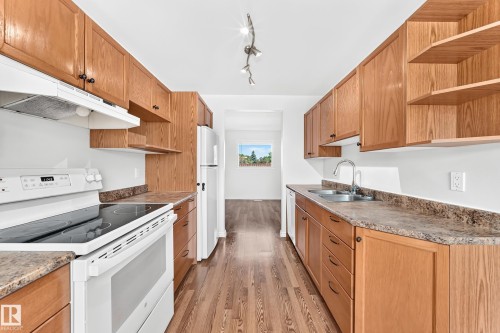 Galley kitchen featuring wood-finish cabinetry, solid surface countertops, white appliances, and wood-finish flooring - 1102 Millbourne Road E, Edmonton, AB 