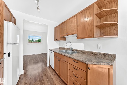 Kitchen featuring wood-finish cabinetry, built-in dishwasher, and a double-basin stainless steel sink with a chrome faucet - 1102 Millbourne Road E, Edmonton, AB 