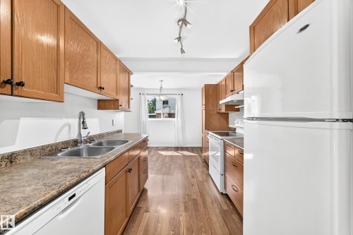 Kitchen featuring wood-finish cabinetry, laminate countertops, a double basin stainless steel sink with chrome faucet, and white appliances including a refrigerator, range, and dishwasher - 1102 Millbourne Road E, Edmonton, AB 