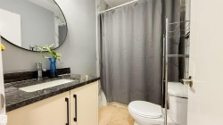 Bathroom featuring a vanity with a dark granite countertop, an undermount sink, and a circular mirror - 