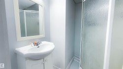 Bathroom featuring a white vanity with an integrated sink, a rectangular framed mirror, and a shower enclosure with frosted glass - 