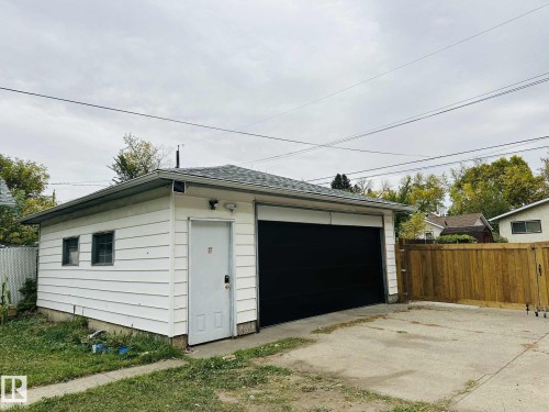 Detached garage featuring white siding, a dark asphalt shingle roof, and a large black garage door - 12005 40 St, Edmonton, AB 