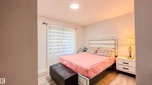 Bedroom featuring wood-finish flooring, a window with horizontal blinds and sheer curtains, a white headboard, and recessed ceiling lighting - 12005 40 St, Edmonton, AB 