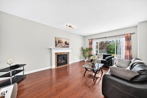 Living area featuring wood-finish flooring, a fireplace with a white mantel and stone surround, and a ceiling-mounted light fixture - 1330 114B Street, Edmonton, AB 