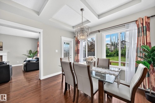 Dining area featuring hardwood flooring, multiple windows, a glass-paneled exterior door, a coffered ceiling, and a crystal chandelier - 1330 114B Street, Edmonton, AB 