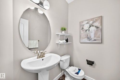 Pedestal sink with brushed nickel faucet, large oval mirror, and wall-mounted light fixture - 1330 114B Street, Edmonton, AB 