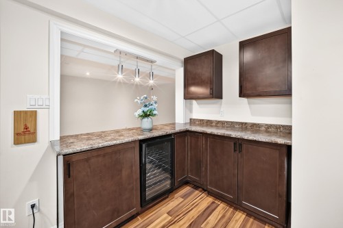 Functional wet bar featuring dark wood-finish cabinetry, a beverage refrigerator, and a stone-look countertop - 1330 114B Street, Edmonton, AB 