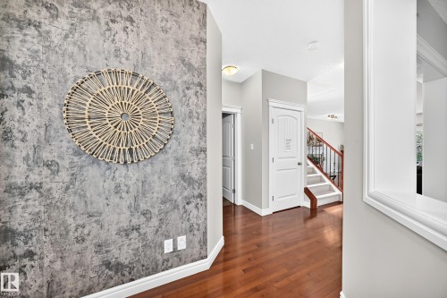 Hallway featuring wood-finish flooring, a textured accent wall, white baseboards, and a white interior door with a paneled design - 1330 114B Street, Edmonton, AB 
