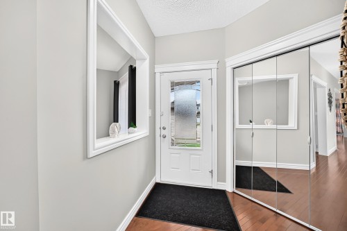 Entryway featuring a white paneled door with decorative glass, wood-finish flooring, light gray walls, an architectural wall niche, and mirrored closet doors - 1330 114B Street, Edmonton, AB 