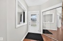 Entryway featuring a white paneled door with decorative glass, wood-finish flooring, light gray walls, an architectural wall niche, and mirrored closet doors - 1330 114B Street, Edmonton, AB 