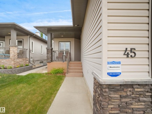 Exterior featuring light-colored horizontal siding, a stone veneer foundation, and a concrete walkway leading to the front entry - 45 Willow Wood Lane, Stony Plain, AB 