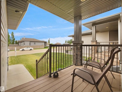 Covered porch featuring wood-finish decking, stone-clad pillars, and dark metal railings - 45 Willow Wood Lane, Stony Plain, AB 