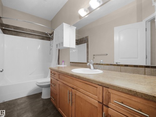 Bathroom featuring a wood-finish vanity with an integrated sink, a large mirror, and tiled flooring - 45 Willow Wood Lane, Stony Plain, AB 