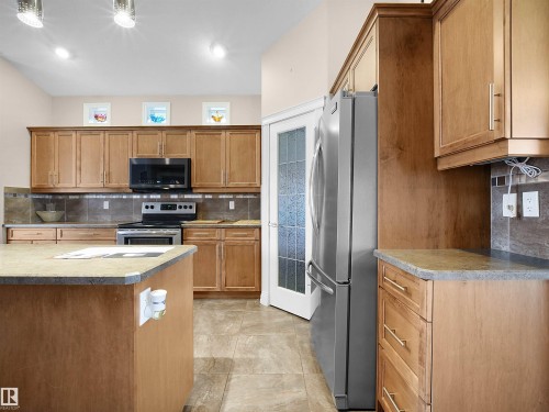 Kitchen featuring wood cabinetry, stainless steel appliances, a center island with countertop, tile flooring, and a tile backsplash - 45 Willow Wood Lane, Stony Plain, AB 