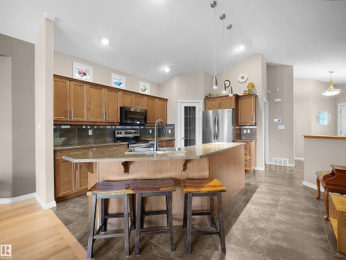 Kitchen featuring a large island with an undermount sink, pendant lighting, stainless steel appliances, wood-finish cabinetry, and tiled flooring - 45 Willow Wood Lane, Stony Plain, AB 