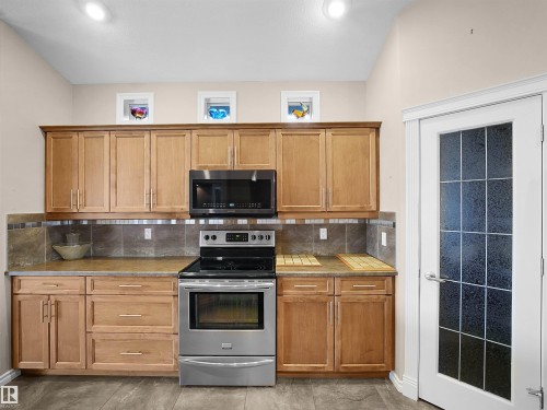 Kitchen featuring light wood-finish cabinetry, stainless steel appliances, a tile backsplash, and wood-finish flooring - 45 Willow Wood Lane, Stony Plain, AB 