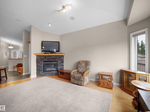 Living area featuring a stone-clad fireplace with a wood mantel, light wood-finish flooring, and a large window with white trim - 45 Willow Wood Lane, Stony Plain, AB 