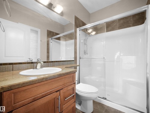 Full bathroom featuring a wood-finish vanity with an integrated sink, a large vanity mirror, a tiled backsplash, and a shower with sliding glass doors - 45 Willow Wood Lane, Stony Plain, AB 