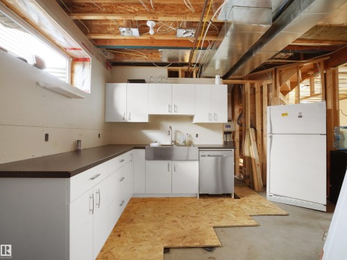 Unfinished basement area featuring a partial kitchen installation with white cabinetry, dark countertops, stainless steel farmhouse sink, and a stainless steel dishwasher - 45 Willow Wood Lane, Stony Plain, AB 
