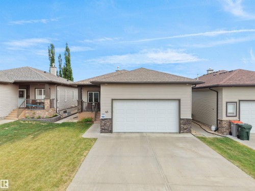 Exterior featuring horizontal siding, a gabled roof, stone accents, an attached garage, and a concrete driveway - 45 Willow Wood Lane, Stony Plain, AB 