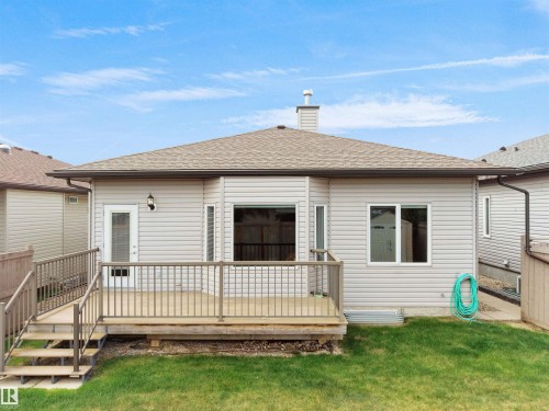 Rear exterior featuring a wood-finish deck with metal railings and steps, light-colored siding, a glass-panel door, and multiple windows - 45 Willow Wood Lane, Stony Plain, AB 