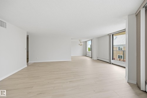 Bright open-concept living area featuring light wood-finish flooring, white painted walls, and multiple large windows - 504 11710 100 Avenue, Edmonton, AB 