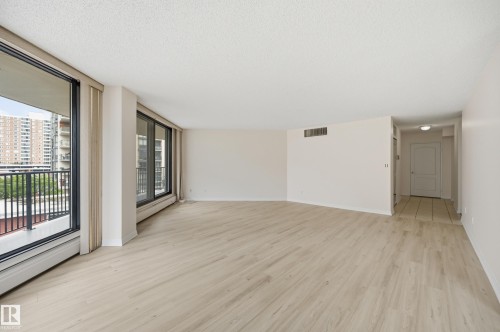 Spacious living area featuring expansive floor-to-ceiling windows, light wood-finish flooring, neutral wall tones, and recessed lighting - 504 11710 100 Avenue, Edmonton, AB 