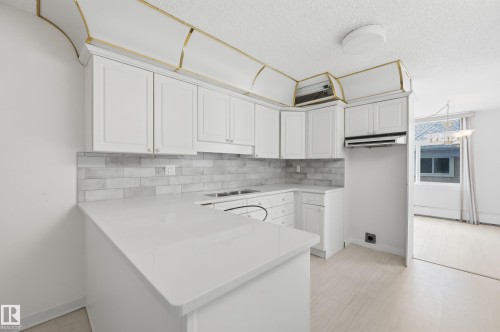 Modern kitchen featuring white shaker cabinetry, light-colored countertops, and a white subway tile backsplash - 504 11710 100 Avenue, Edmonton, AB 