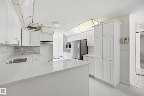 Kitchen featuring white shaker-style cabinetry, a white countertop island, stainless steel appliances, a subway tile backsplash, and light-toned flooring - 504 11710 100 Avenue, Edmonton, AB 