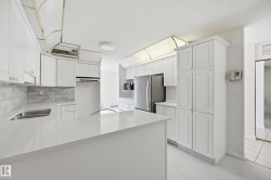 Kitchen featuring white shaker-style cabinetry, a white countertop island, stainless steel appliances, a subway tile backsplash, and light-toned flooring - 