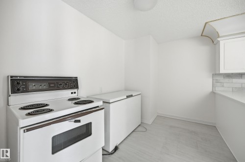 Kitchenette featuring an electric range, white cabinetry, a light-toned countertop, and a subway tile backsplash - 504 11710 100 Avenue, Edmonton, AB 