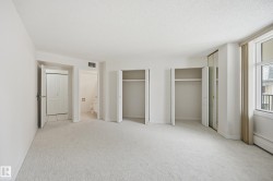 Light-colored carpeting throughout, featuring two open closet spaces, a mirrored closet door, and a large window with a balcony visible - 
