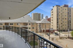 Curved balcony with black metal railings, offering urban views of surrounding multi-story buildings - 