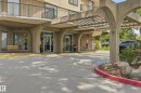 Building entrance featuring a covered drive-up area with a concrete pergola structure, multiple glass entrance doors, and an exterior balcony with black railings - 504 11710 100 Avenue, Edmonton, AB 
