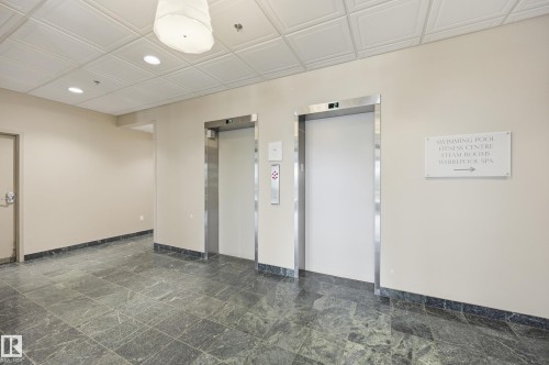 Lobby area featuring two elevators with stainless steel frames, recessed lighting, and a prominent ceiling light fixture - 504 11710 100 Avenue, Edmonton, AB 