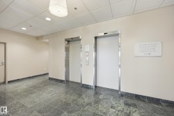 Lobby area featuring two elevators with stainless steel frames, recessed lighting, and a prominent ceiling light fixture - 