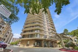 High-rise condominium building featuring a curved architectural design, individual balconies with black railings, a covered entrance, and mature tree landscaping - 
