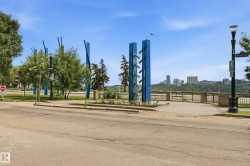 Paved pathway featuring ornamental blue pillars, lush greenery, and a distant cityscape under a clear sky - 