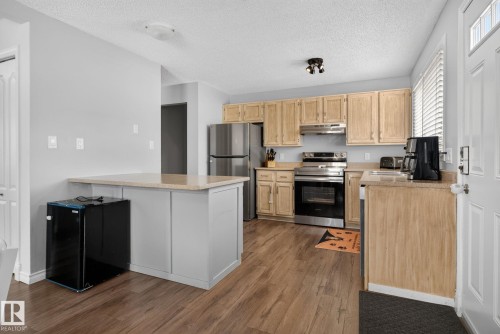 Open-concept kitchen featuring wood-finish flooring, light wood cabinetry, stainless steel appliances, a breakfast bar, and light-toned countertops - 3218 41 Street, Leduc, AB 