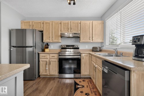 Kitchen featuring wood-finish flooring, light-toned cabinetry, stainless steel appliances, a double basin sink, and ample countertop space - 3218 41 Street, Leduc, AB 