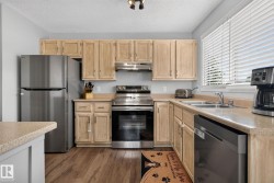 Kitchen featuring wood-finish flooring, light-toned cabinetry, stainless steel appliances, a double basin sink, and ample countertop space - 