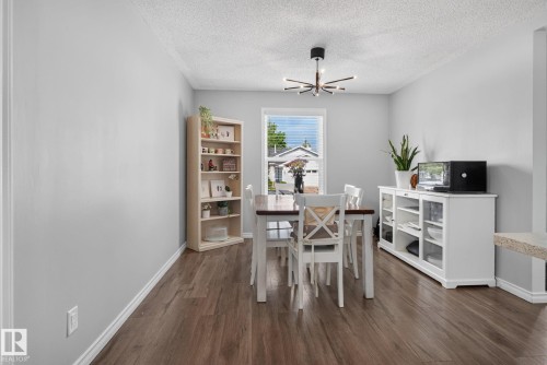 Dining area featuring wood-finish flooring, a contemporary ceiling light fixture, a window with blinds, and light gray wall paint - 3218 41 Street, Leduc, AB 