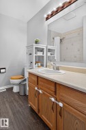 Bathroom featuring wood-finish flooring, a wood vanity with a white countertop, and a large wall mirror - 