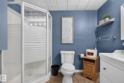 Corner shower enclosure with frosted glass panels, white basin vanity with storage, tile flooring, blue wall paint, and a pressed tin ceiling - 
