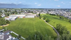 Expansive green space featuring a paved walking path, mature trees, and a community building with a large sports field - 