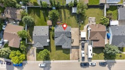 Aerial view of a residential property featuring a paved driveway, a large rear yard with a patio, mature trees, and a shingle roof - 