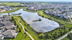 Expansive residential community with a central lake featuring a walking path, mature landscaping, and numerous properties with private decks - 