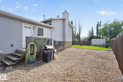 Backyard featuring a gravel patio area, wooden deck with stairs, a white exterior door, and a white storage shed - 3218 41 Street, Leduc, AB 