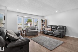 Open-concept living area featuring wood-finish flooring, a bay window with blinds, recessed ceiling lighting, and light gray wall paint - 